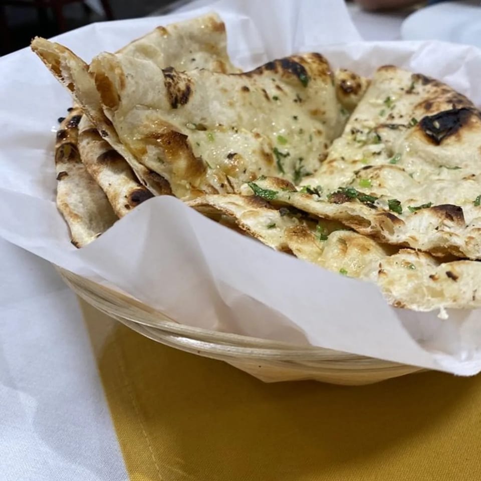 A basket of warm, garlic naan bread from Heart of India, lined with white paper.