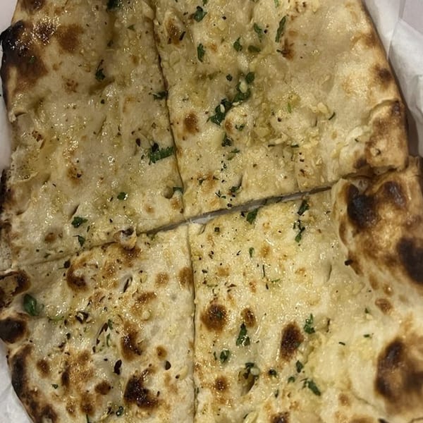 Close-up of Heart of India's garlic naan, glistening with butter and sprinkled with herbs.