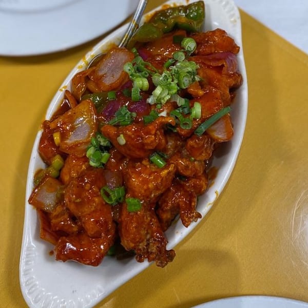 Heart of India's chili chicken, a vibrant dish with red sauce, green peppers, and onions.