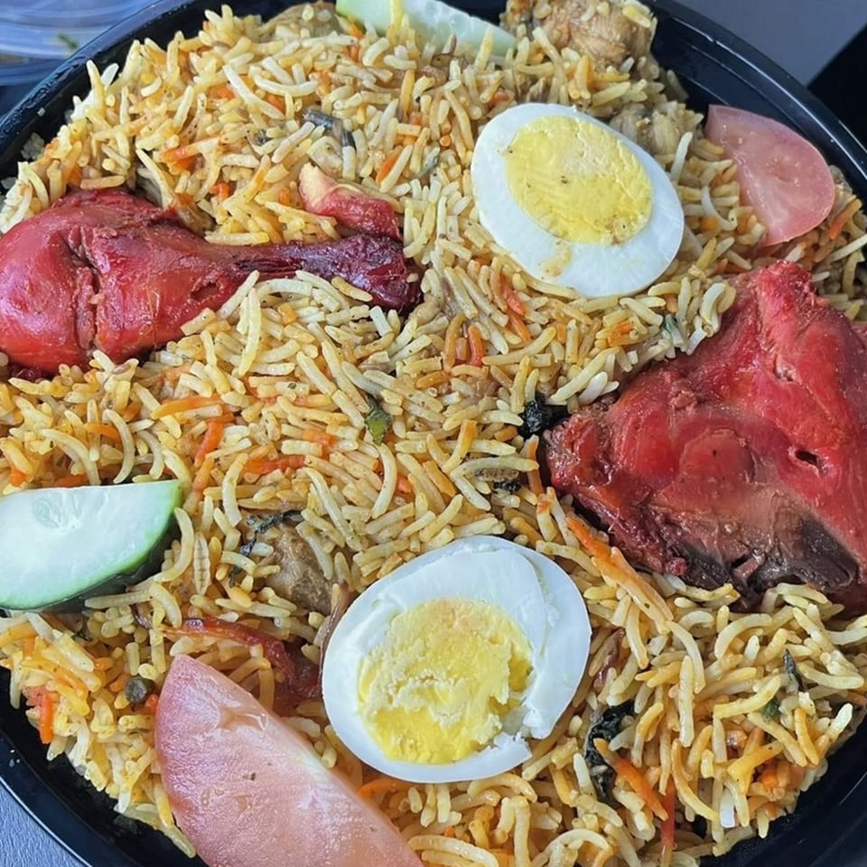 Heart of India's chicken biryani with red chicken pieces, boiled eggs, and vegetable garnishes.