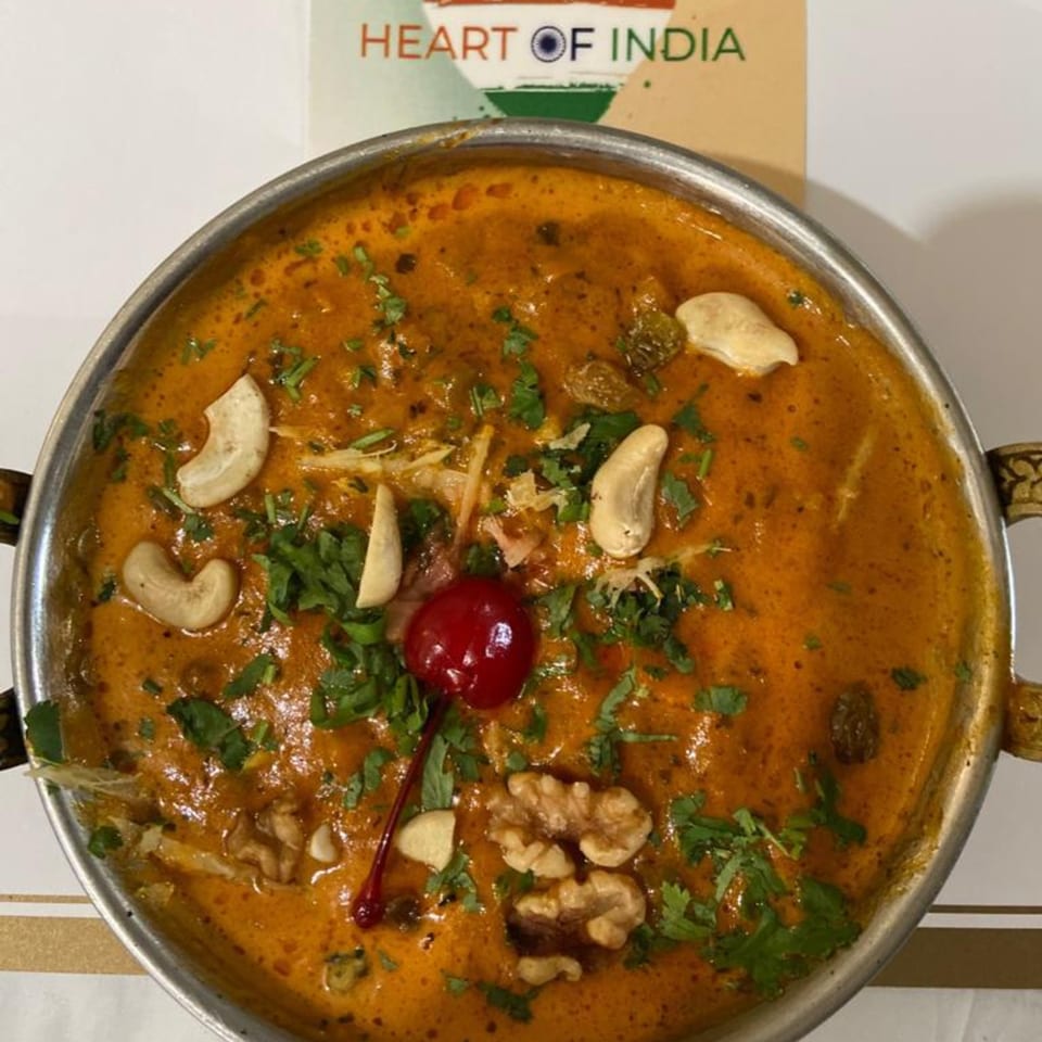 Heart of India's creamy Indian curry, garnished with cashews, walnuts, cilantro, and a cherry.